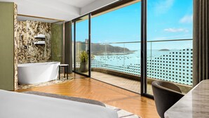 Une salle de bain moderne avec une baignoire sur pieds, une douche séparée par des parois en verre et une grande fenêtre donnant sur la mer.
