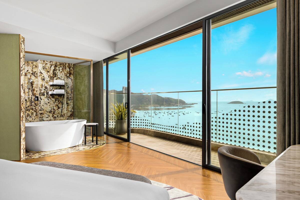 Ein modernes Badezimmer mit freistehender Badewanne, einer in Glas eingefassten Dusche und einem großen Fenster mit Meerblick.
