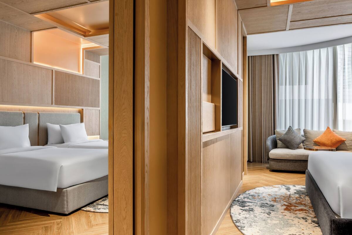Ein Hotelzimmer mit Bett, einer Couch, einem Fernseher und einem großen Fenster mit Vorhängen.