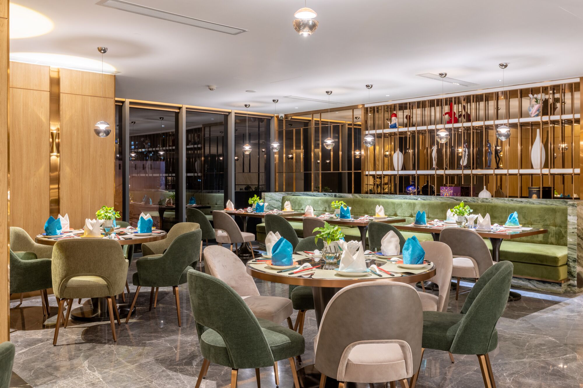 A modern restaurant interior with round tables, green upholstered chairs, and a bar area with a green sofa.