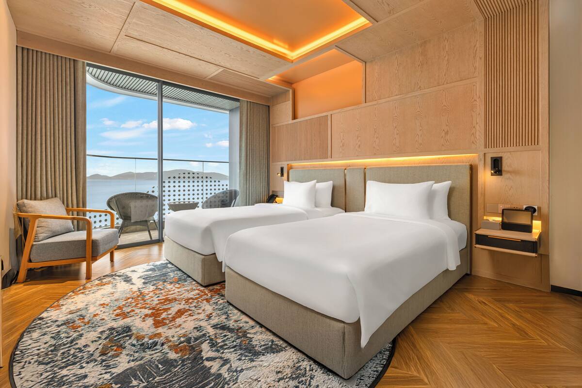 Ein Hotelzimmer mit zwei Betten, einem großen Fenster mit Blick, Holzboden und modernem Design.