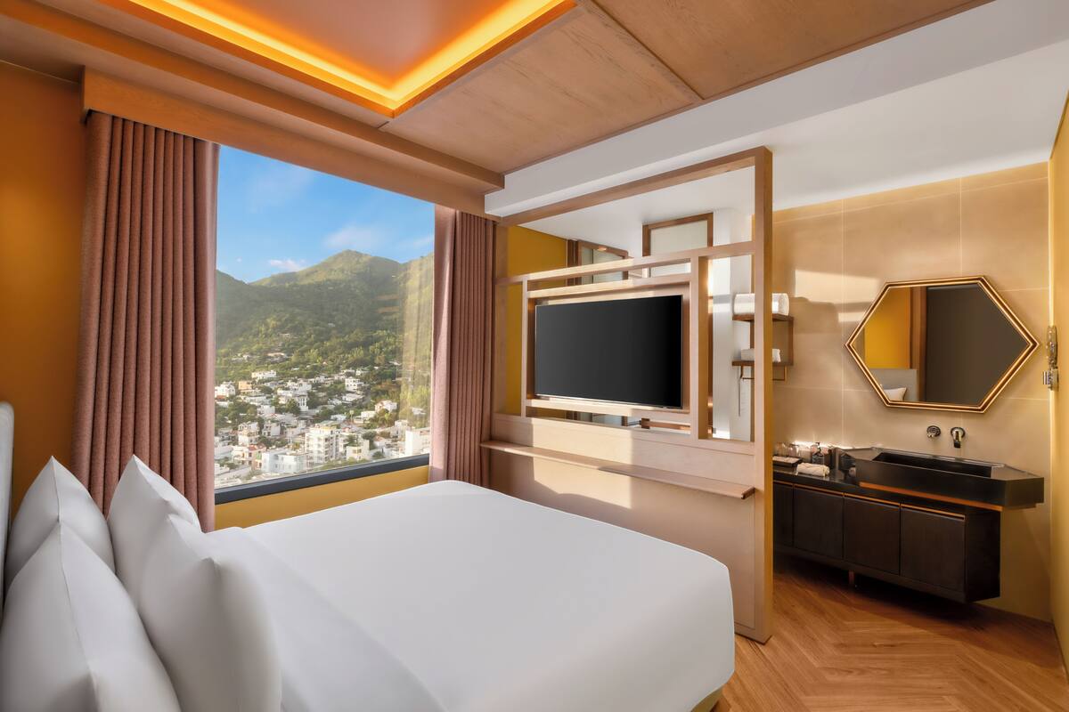 Ein Hotelzimmer mit Bett, Fernseher und Badezimmer mit Waschbecken, mit Blick auf die Berge.