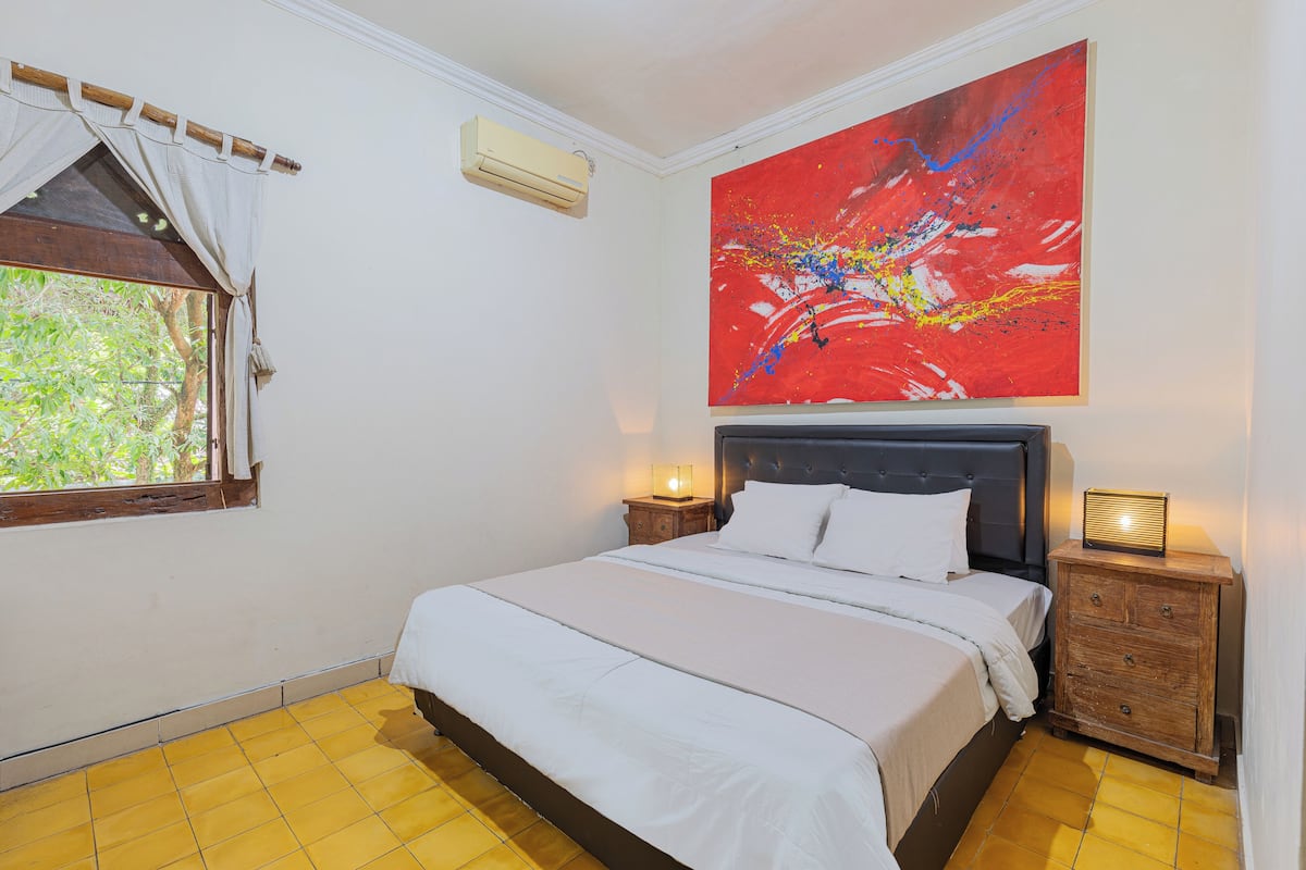 A bedroom with a bed, a nightstand, a dresser, a window with curtains, and a large abstract painting on the wall.