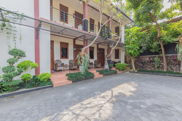 A building with a covered porch, potted plants, and a paved courtyard.
