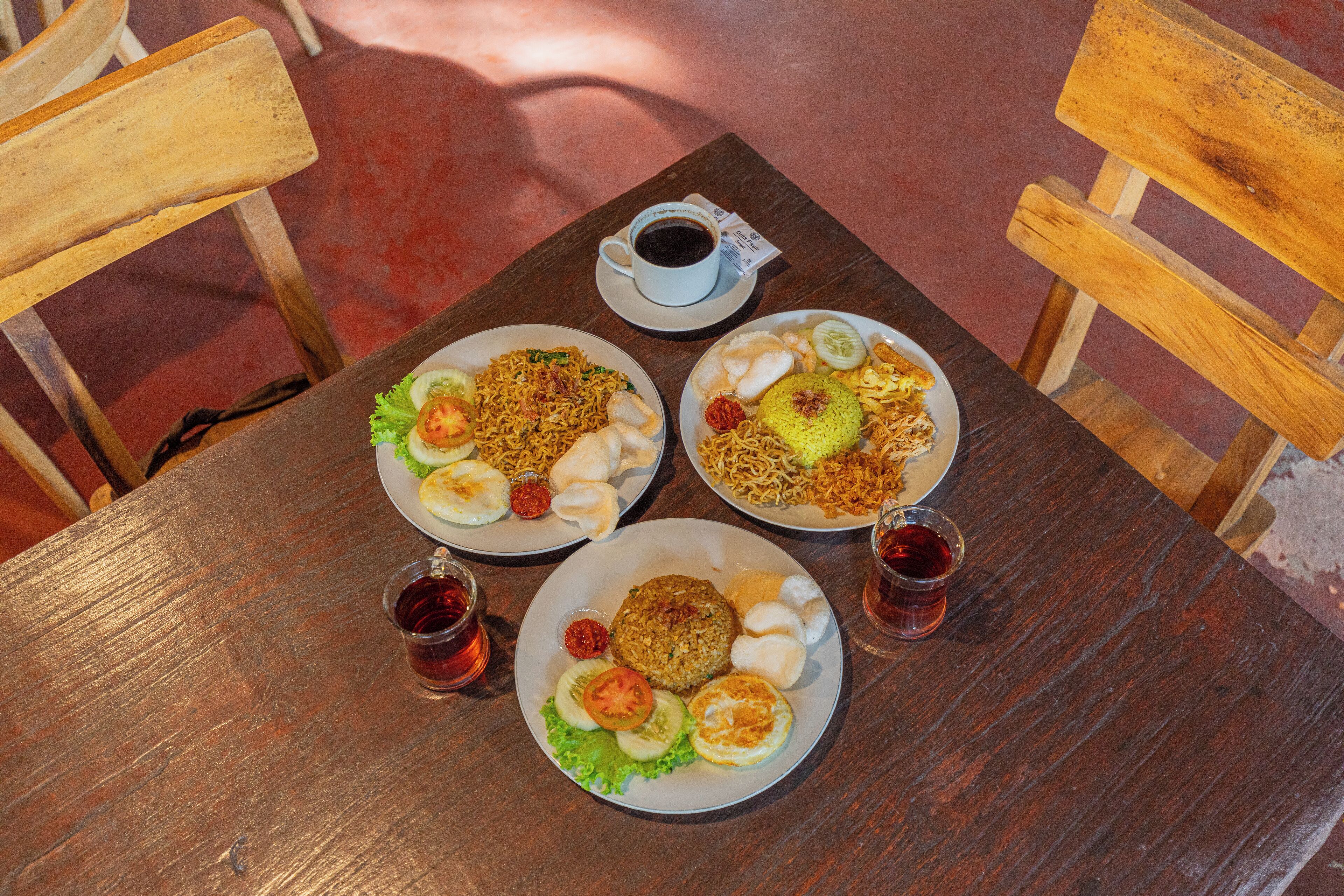 A wooden table with three plates of food, a cup of coffee, and two glasses of tea.