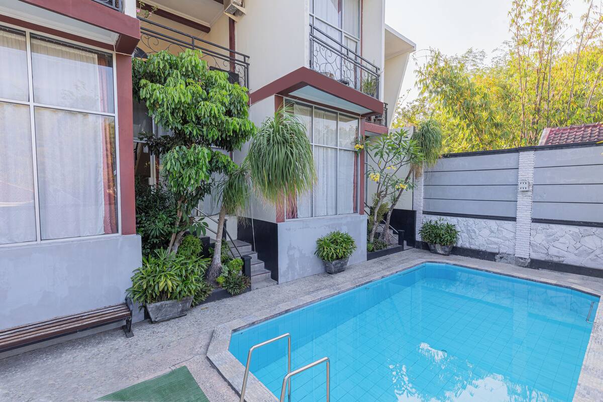 A swimming pool with a tiled edge, surrounded by potted plants and a bench.