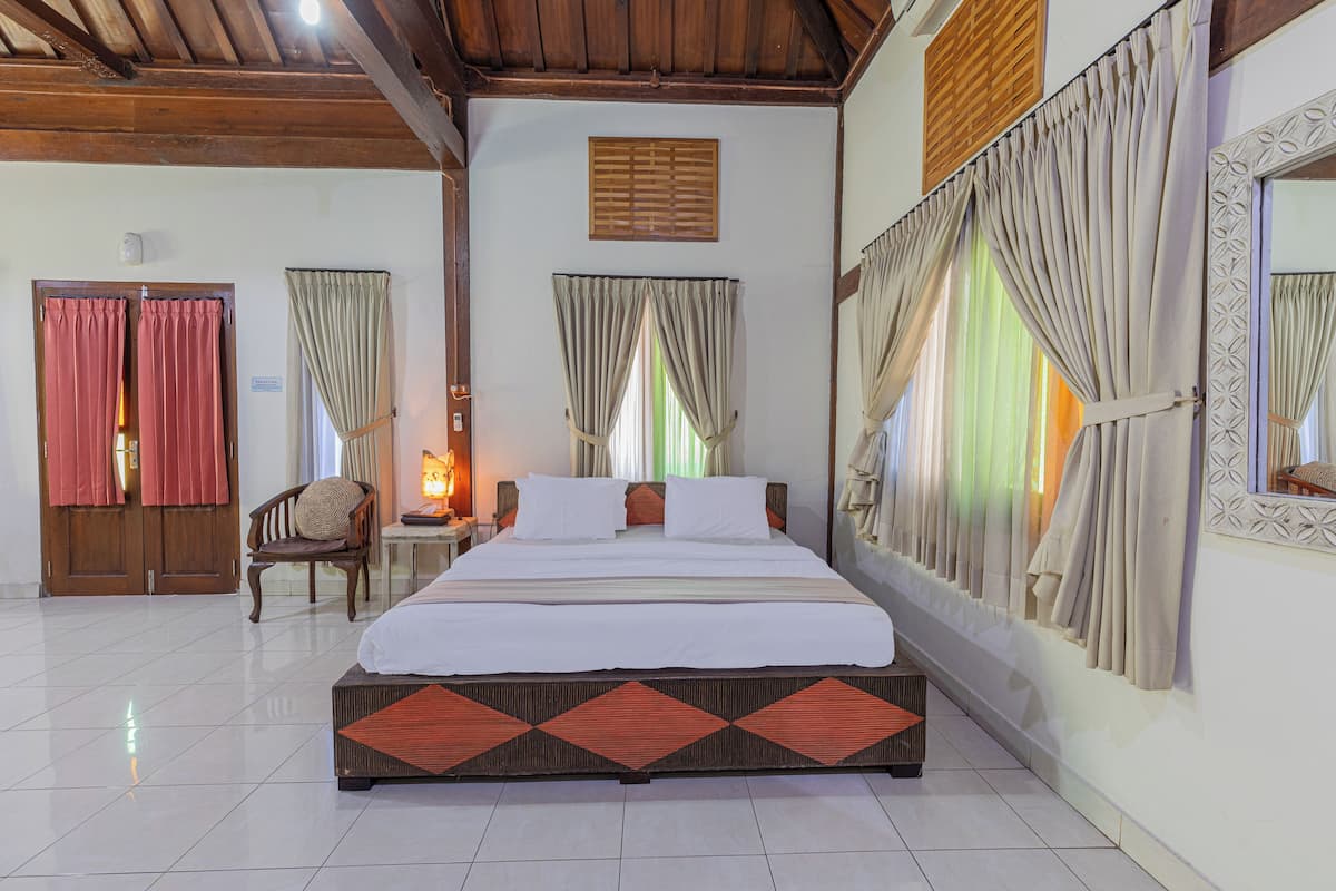 A hotel room with a large bed, wooden ceiling, and curtains on the windows.