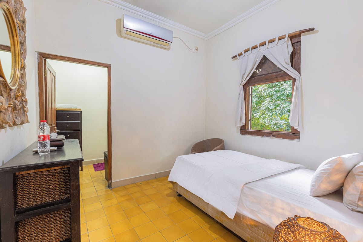 A bedroom with a bed, a dresser, a mirror, an air conditioner, and a window with a view of greenery.
