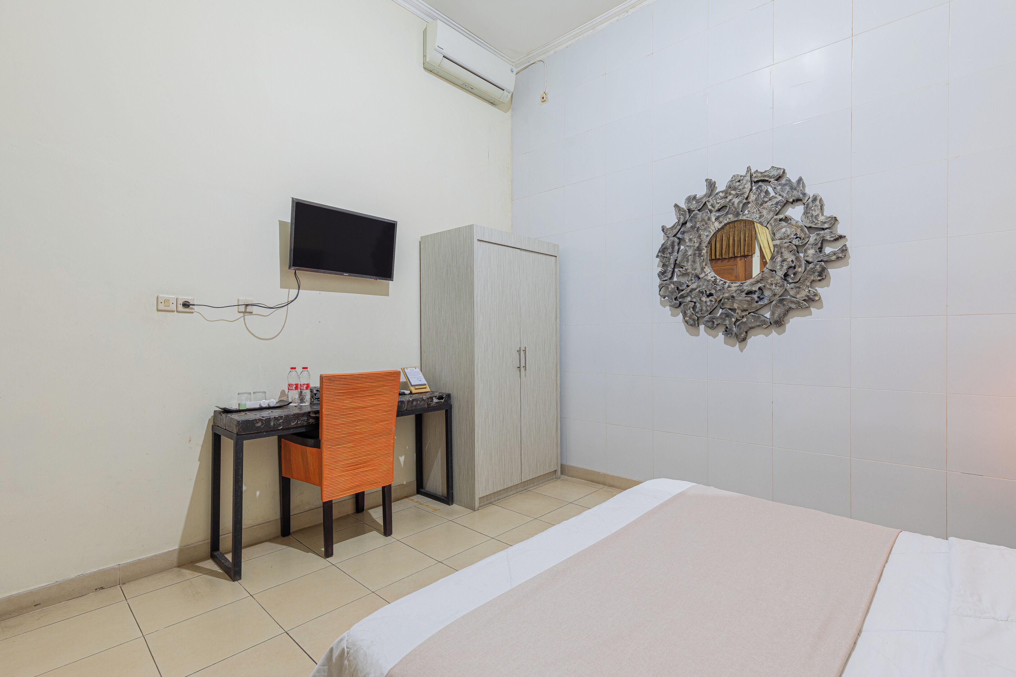 Una habitación de hotel con una cama, un escritorio con silla, un televisor y un espejo decorativo.
