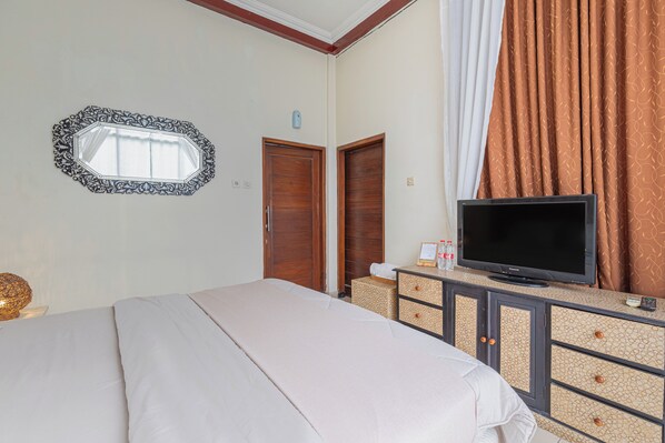 A hotel room with a bed, a television on a dresser, a mirror, and two doors. - Pondok Gajah Hotel (Kasihan)