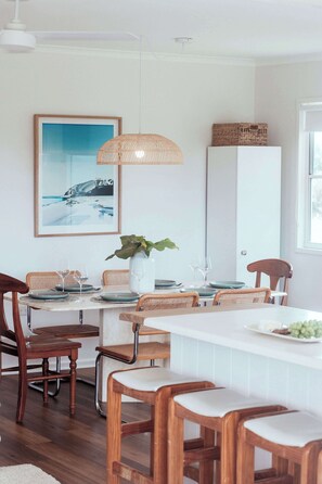Un comedor con una mesa blanca, sillas de mimbre y una lámpara colgante.