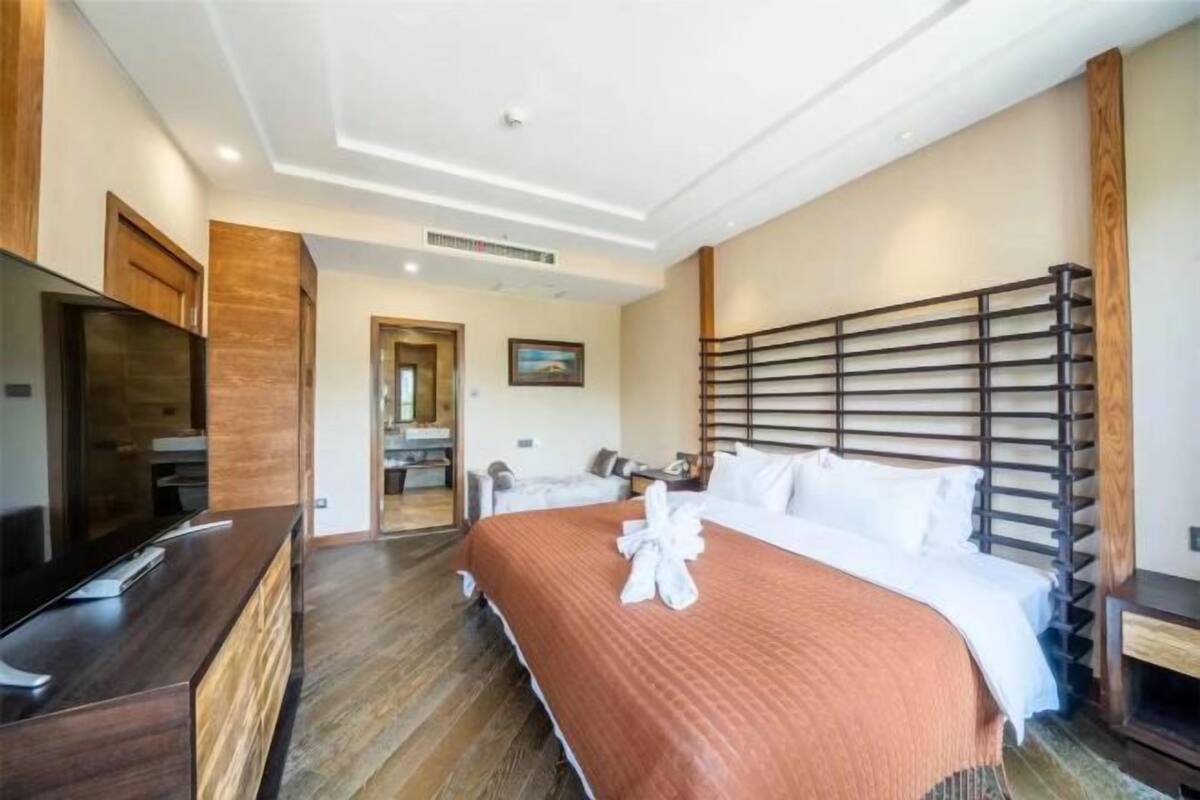 A hotel room with a large bed, a TV, a wooden desk, and a bathroom visible through an open door.
