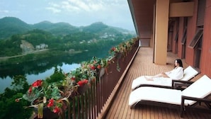 A balcony with a wooden floor, two white lounge chairs, and a view of a lake and mountains. - Geheyan Hotel (Changyang)
