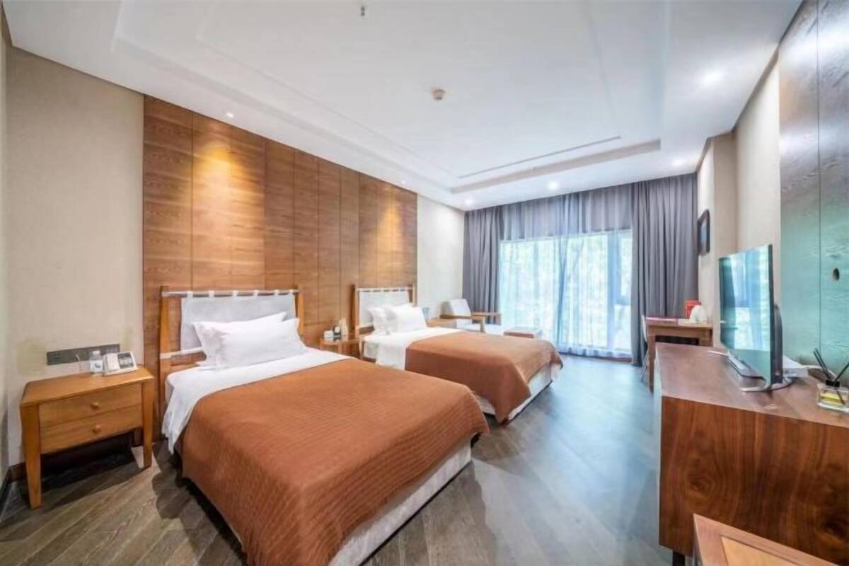 A hotel room with two beds, wooden paneling on the walls, a desk with a computer, and a large window with curtains.