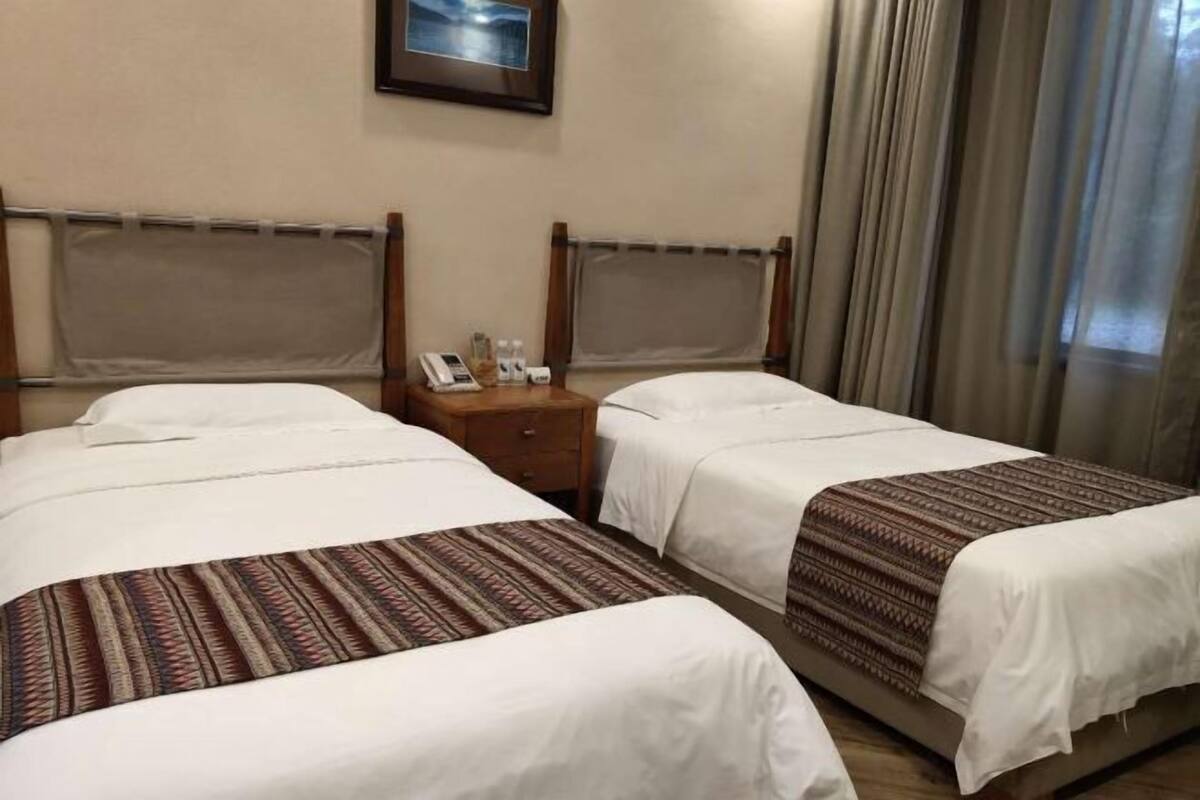 A hotel room with two beds, a nightstand with a phone and toiletries, and a framed picture on the wall.