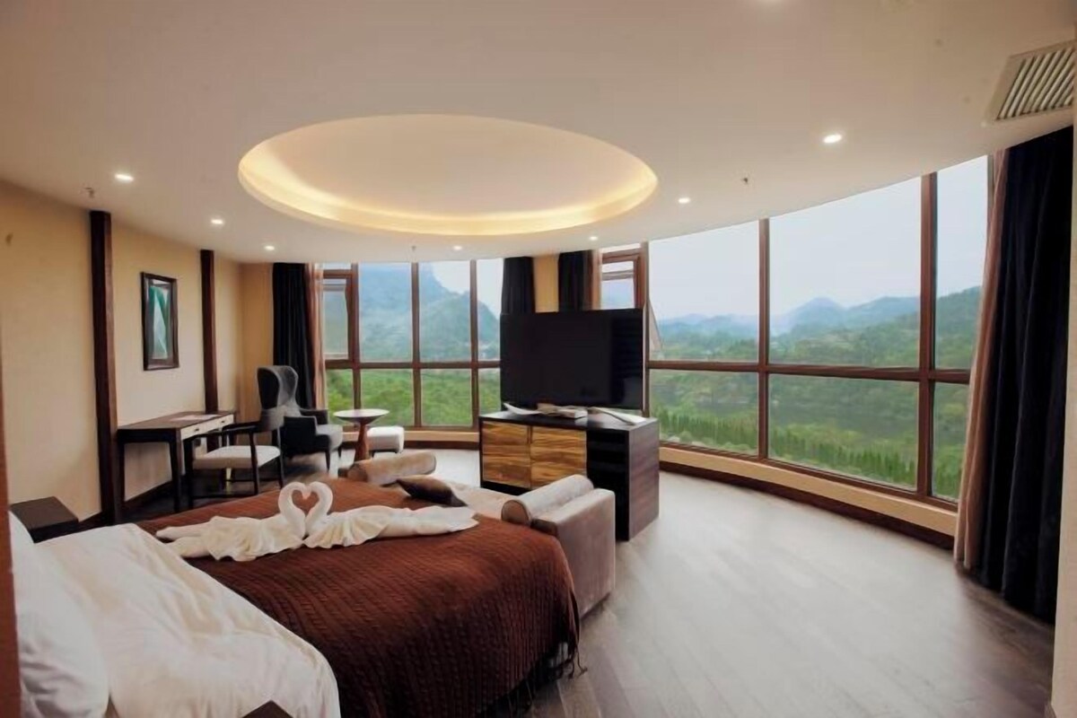 A hotel room with a large bed, a desk, a TV, and a view of the mountains.