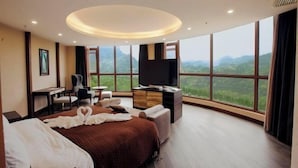A hotel room with a large bed, a desk, a TV, and a view of the mountains. - Geheyan Hotel (Changyang)