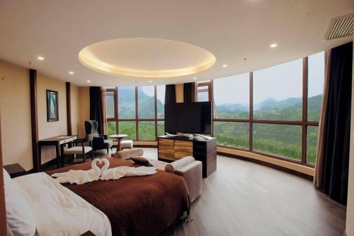 A hotel room with a large bed, a desk, a TV, and a view of the mountains.