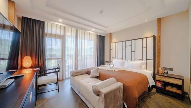 A modern hotel room with a large bed, a sofa, a desk with a lamp, and a TV. - Geheyan Hotel (Yichang)
