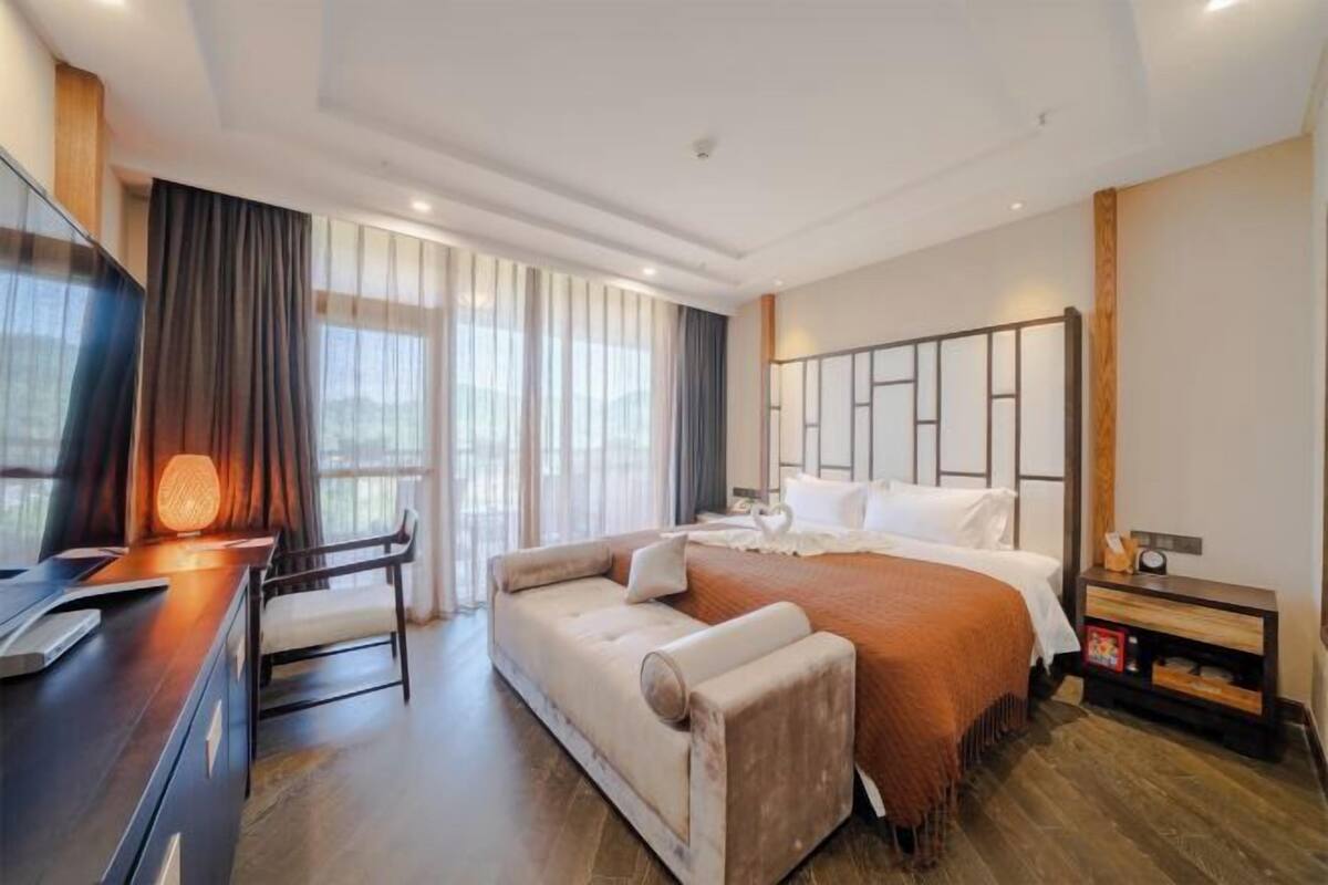 A modern hotel room with a large bed, a sofa, a desk with a lamp, and a TV.
