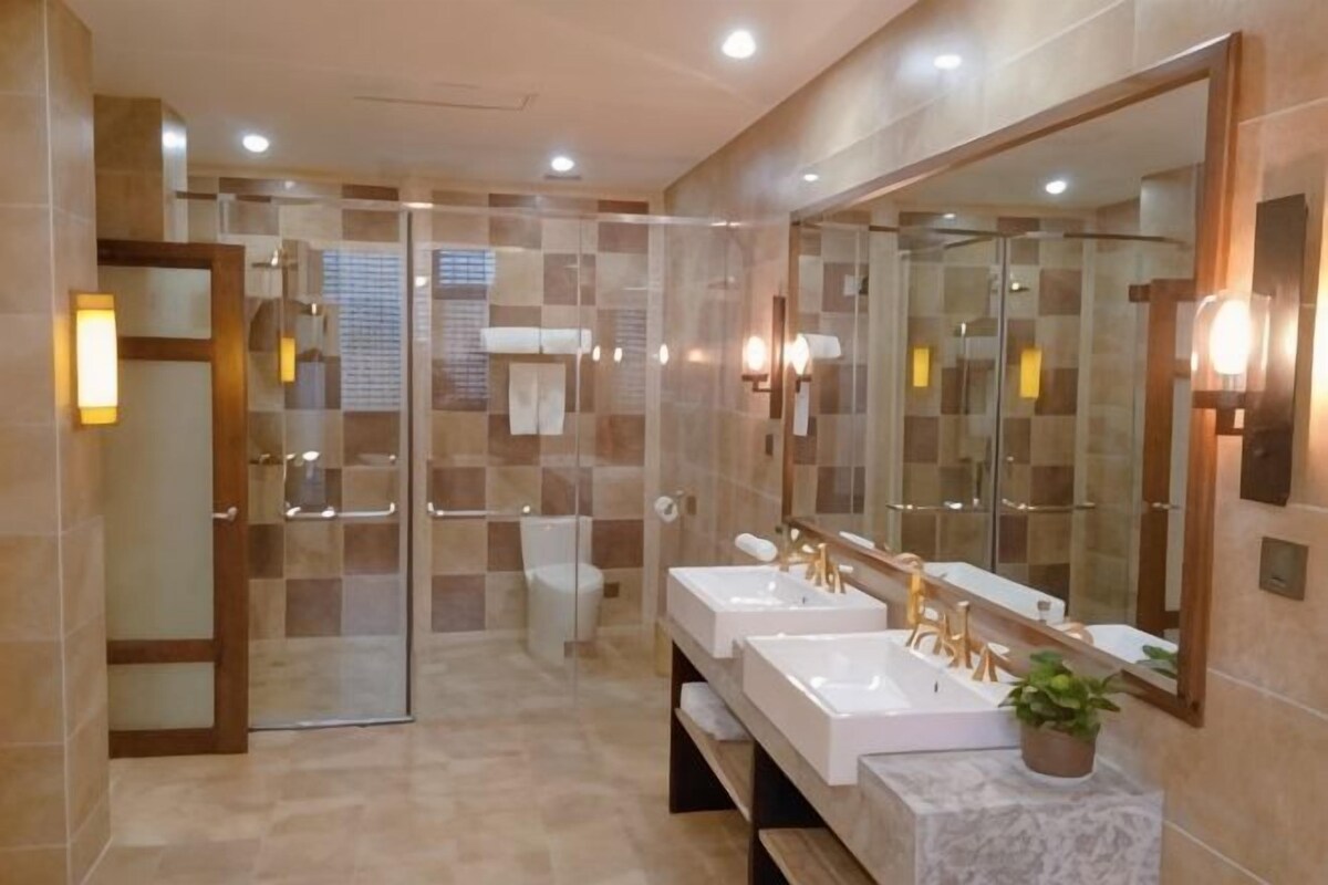 A modern bathroom with a glass shower enclosure, two sinks with gold fixtures, and a large mirror.