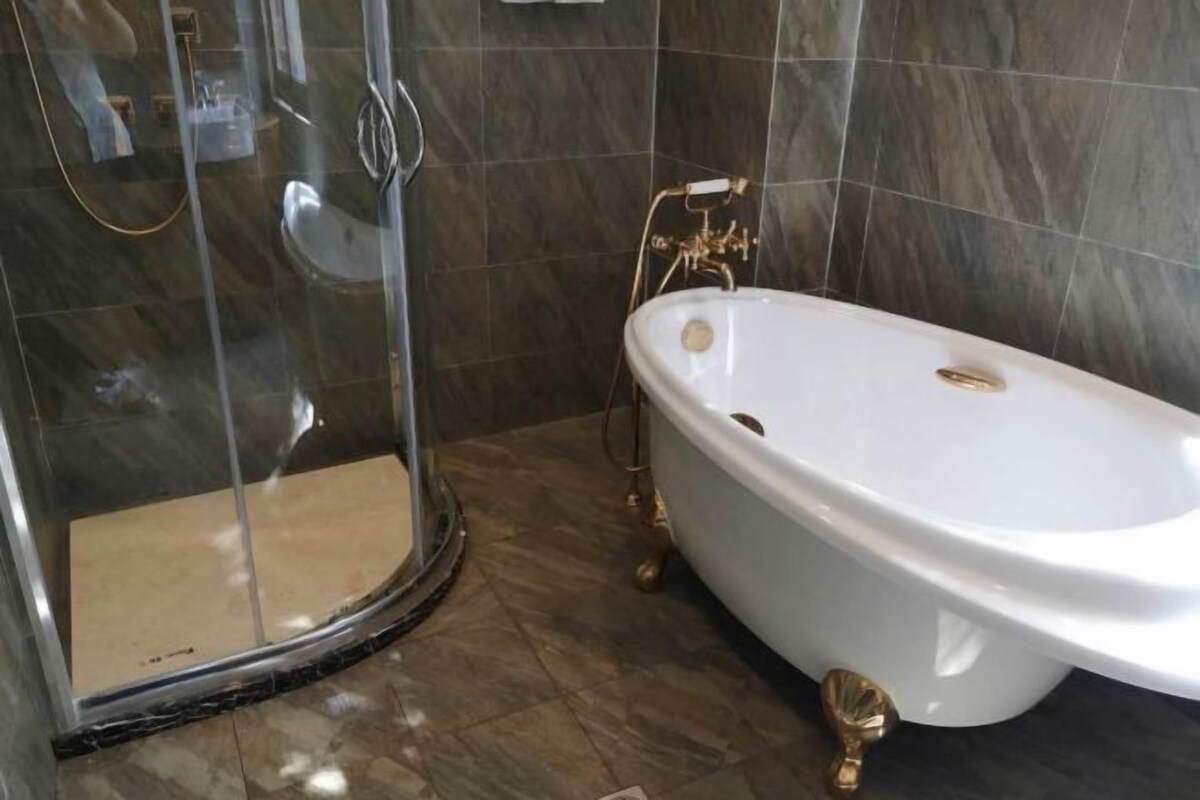 A bathroom with a white bathtub, a glass shower enclosure, and dark tiled walls.