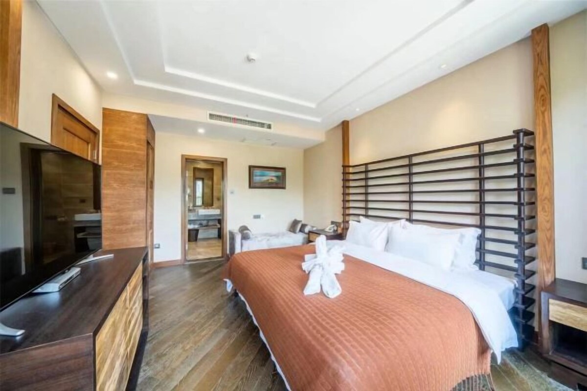 Ein Hotelzimmer mit einem großen Bett, einem Fernseher, einem Holztisch und einem durchgehenden Türbogen einsehbaren Badezimmer.