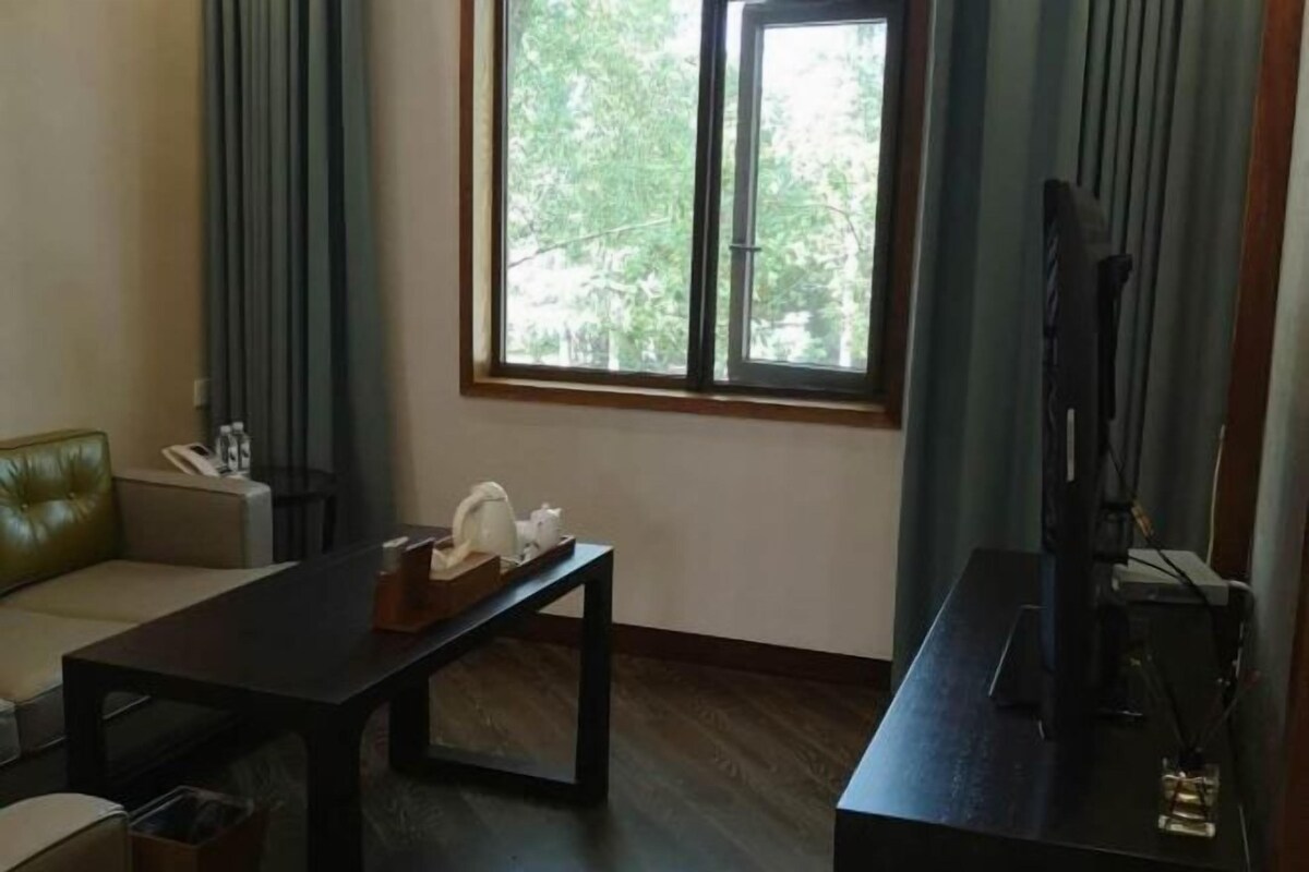 A room with a sofa, a table with a tray, a television, and a window with curtains.