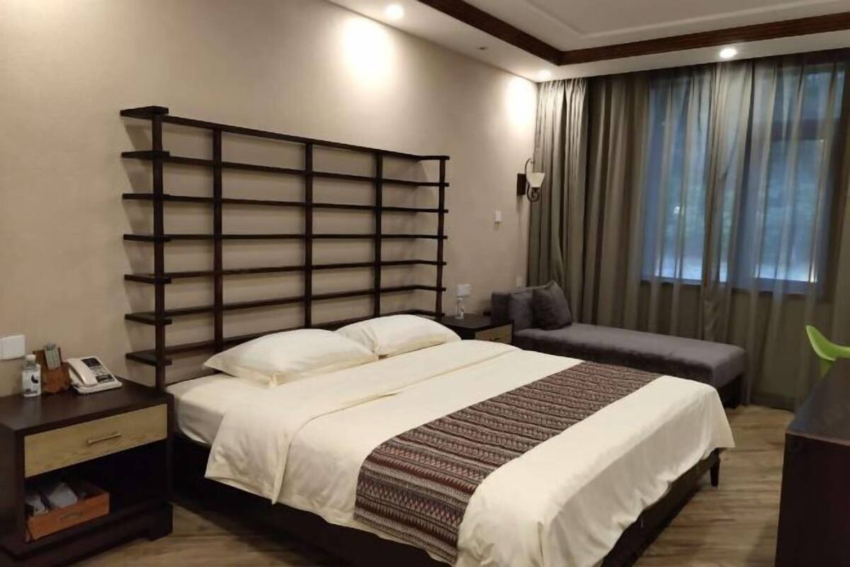 A hotel room with a large bed, a bedside table with a lamp, a small desk, and a chair.