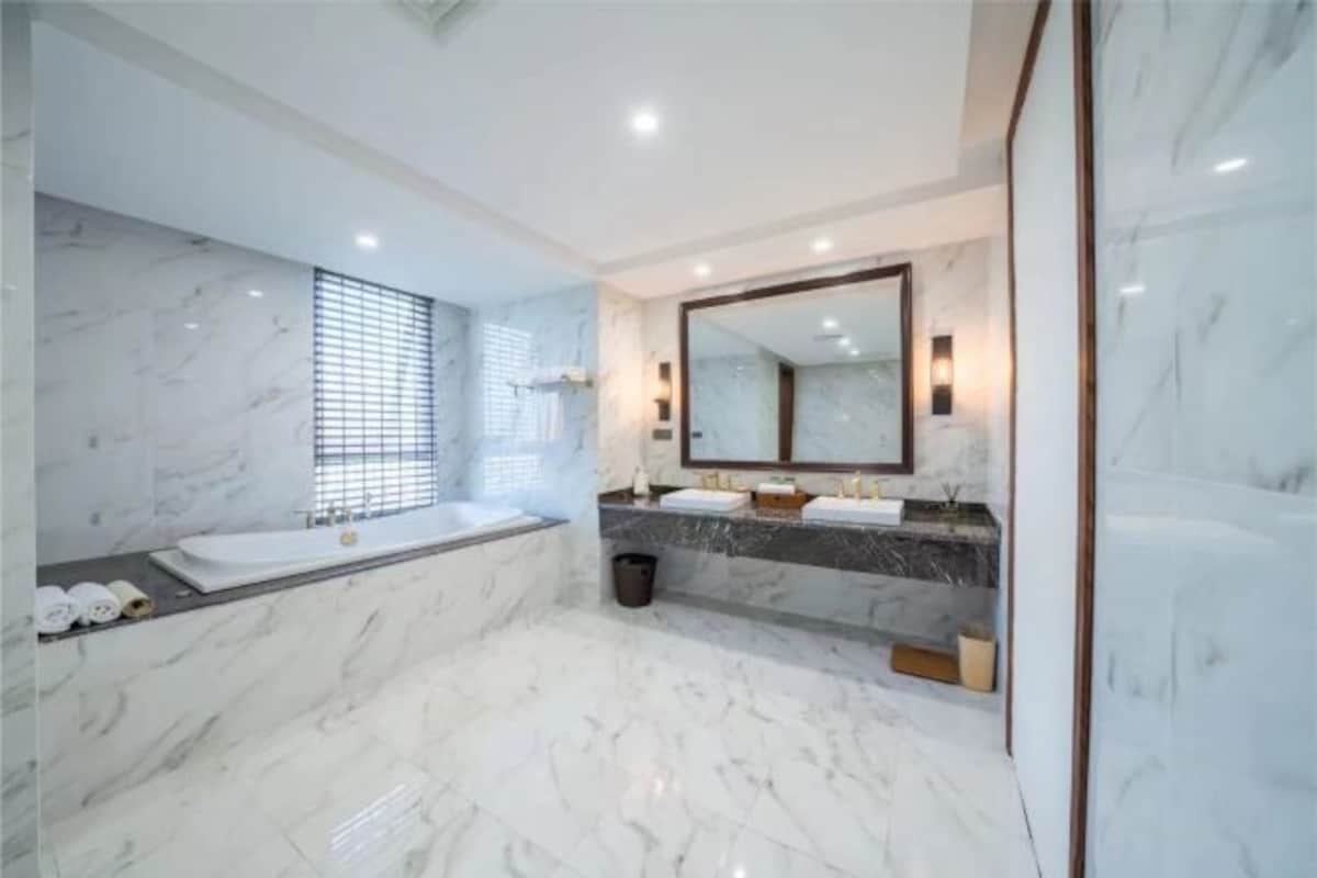 A modern bathroom with marble floors, a large mirror, two sinks, and a bathtub.