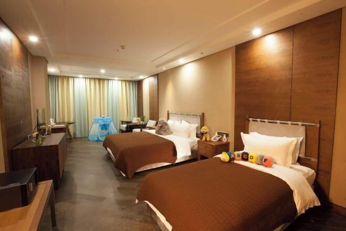 A hotel room with two beds, a desk, a chair, a nightstand, and a window with curtains.