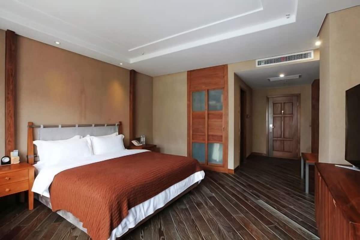 A hotel room with a large bed, a nightstand, a TV, and a wooden floor.