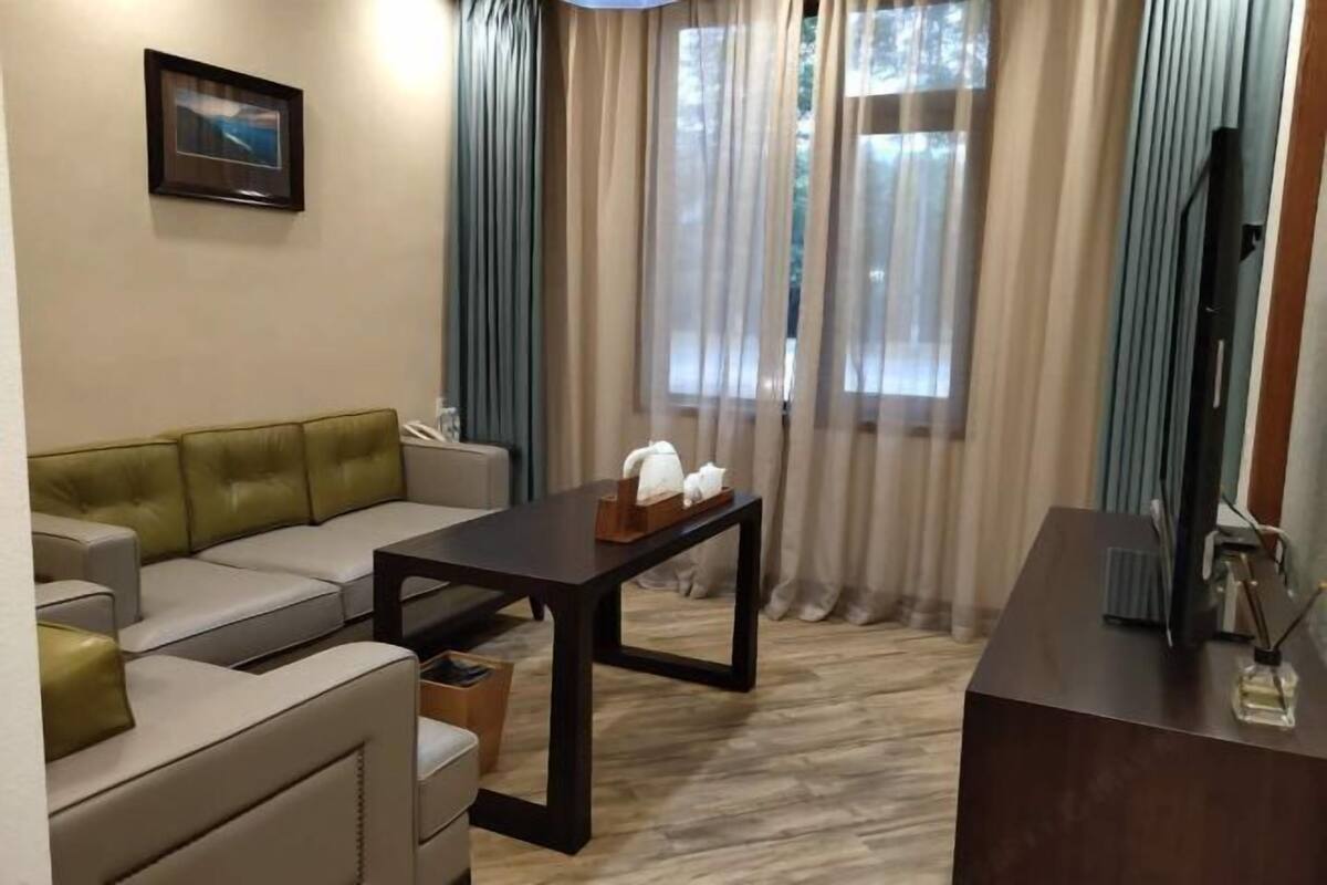 A living room with a sofa, a coffee table, a TV, and a window with curtains.