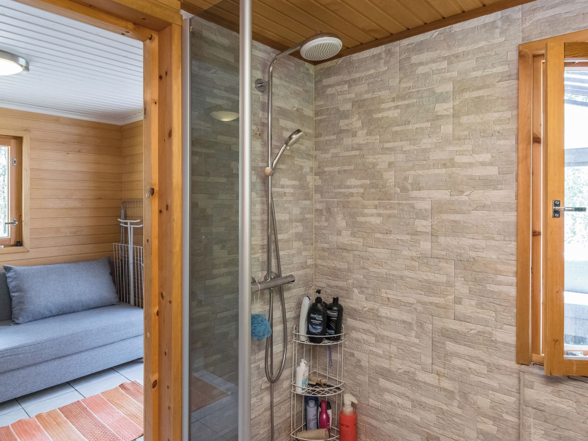 A shower area with a glass door, a wooden bench, and a shelf with toiletries.