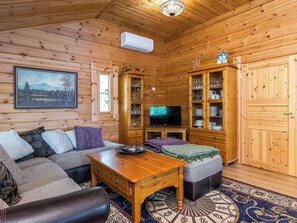 Interior acogedor de una cabaña de madera, con un sofá, un televisor y un mueble con puertas de cristal.