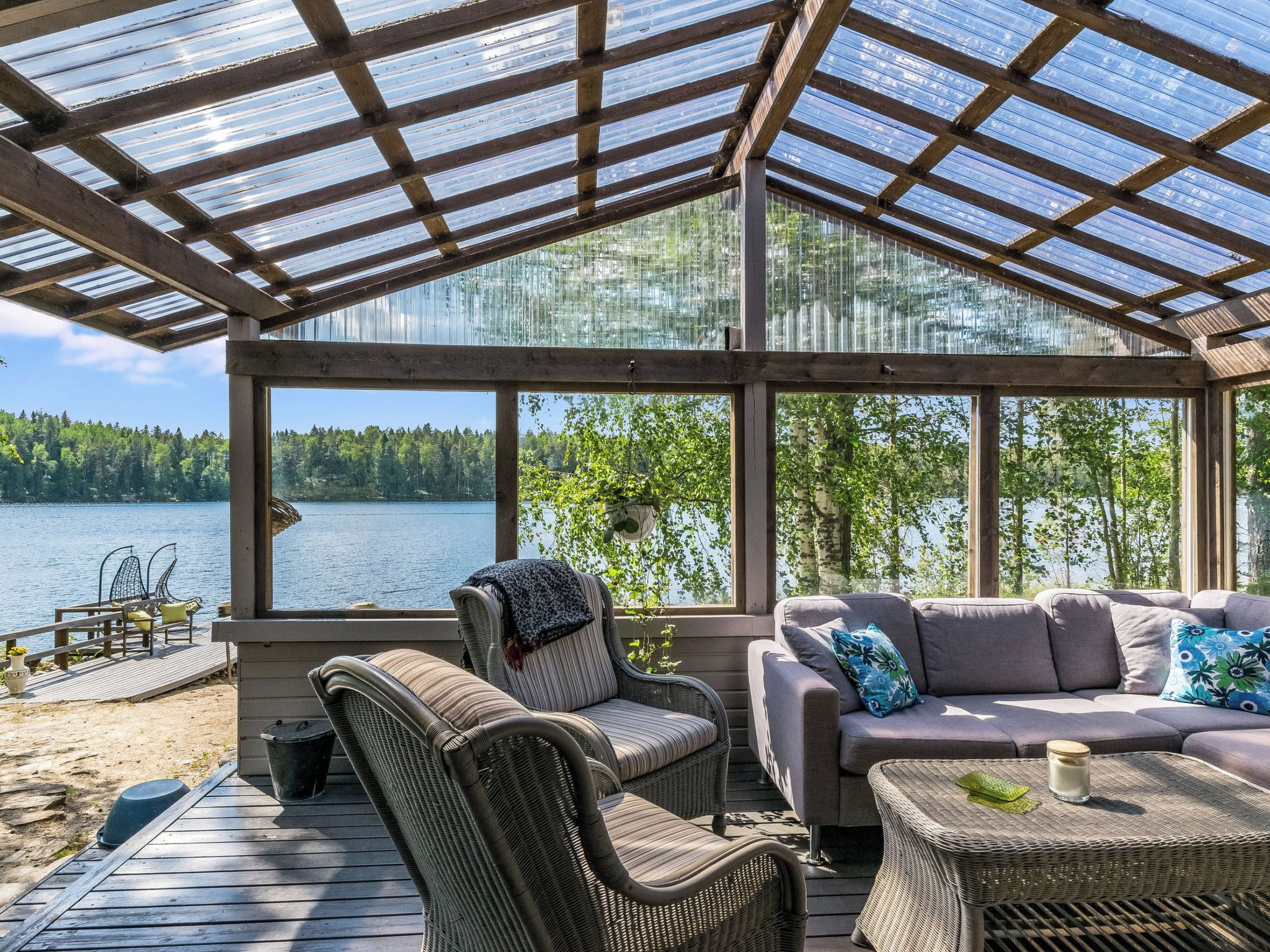 A covered outdoor deck with wicker furniture, a view of a lake, and a forest in the background.