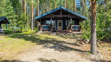 A cabin with a porch, surrounded by tall trees.