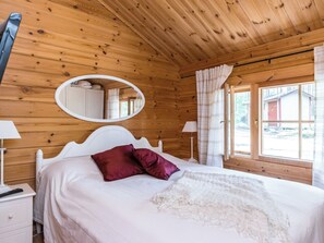 Un dormitorio de cabaña de madera con una cama, una mesita de noche, un espejo y una ventana.