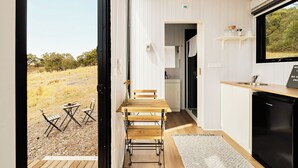 A modern kitchen with a wooden table and chairs, a black refrigerator, and a window overlooking a natural landscape.