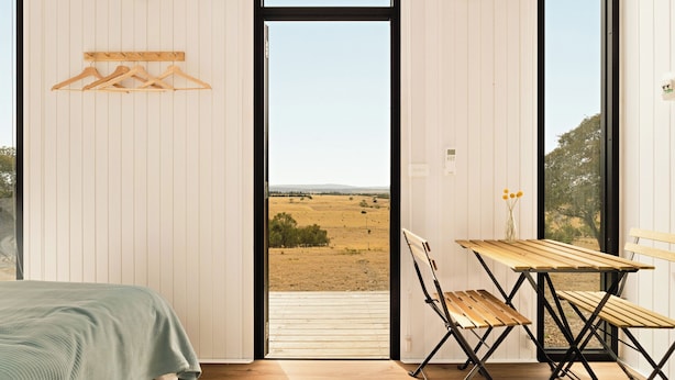 A room with a bed, a table with chairs, a view through a large window, and a wall-mounted coat rack.