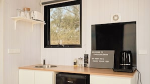A kitchen with a sink, a Hisense dishwasher, a window with a view of trees, a shelf with kitchen items, and a welcome sign.
