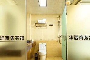 Une petite salle de bain carrelée, avec des toilettes, une étagère au-dessus du lavabo et un espace douche.