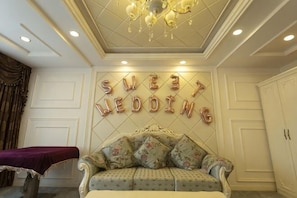 A room with a sofa, a chandelier, and a wall with 'SWEET WEDDING' letters.