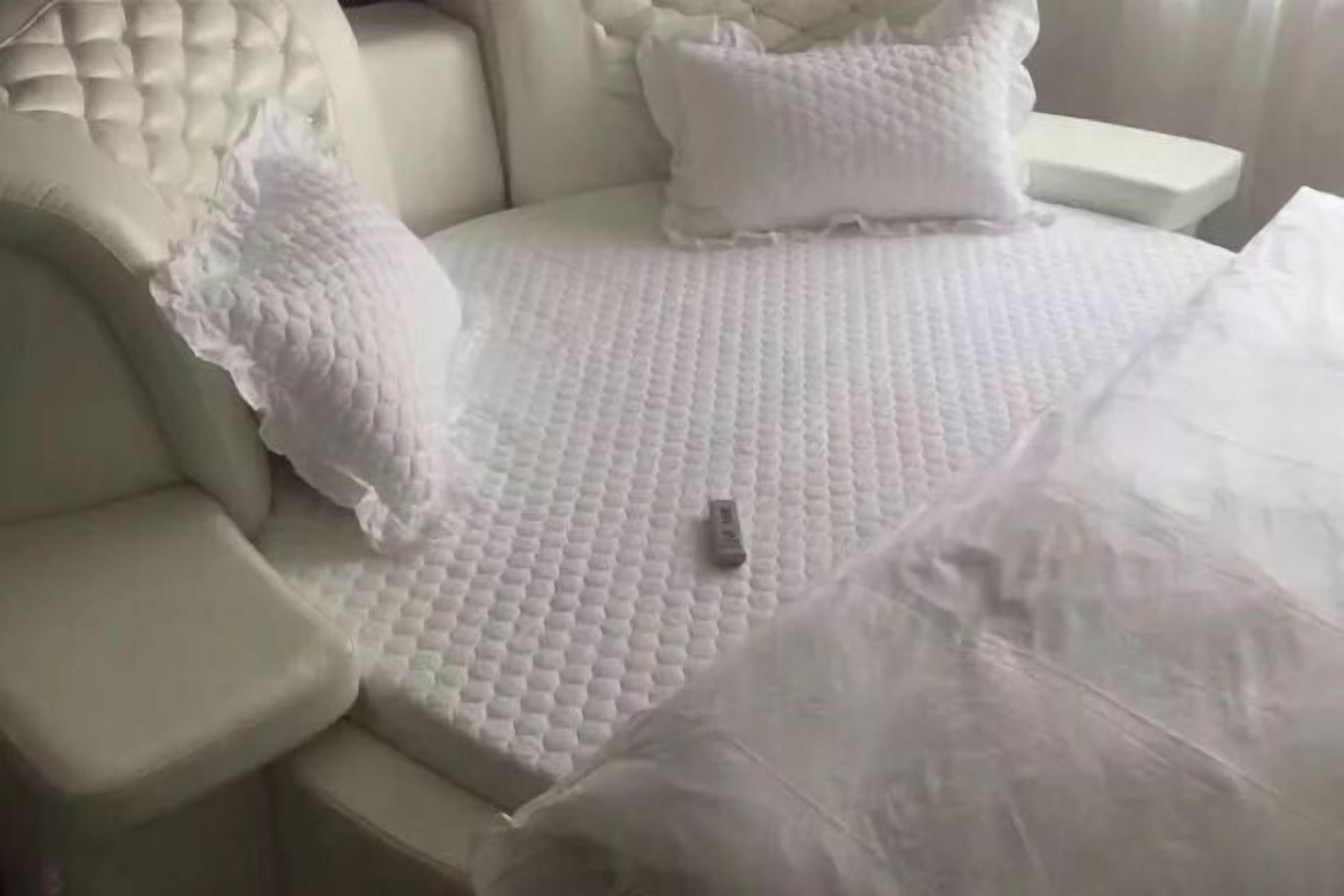 Cabecera blanca con vetas y una colcha blanca con textura, además de almohadas.