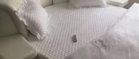 Cabecera blanca con vetas y una colcha blanca con textura, además de almohadas.