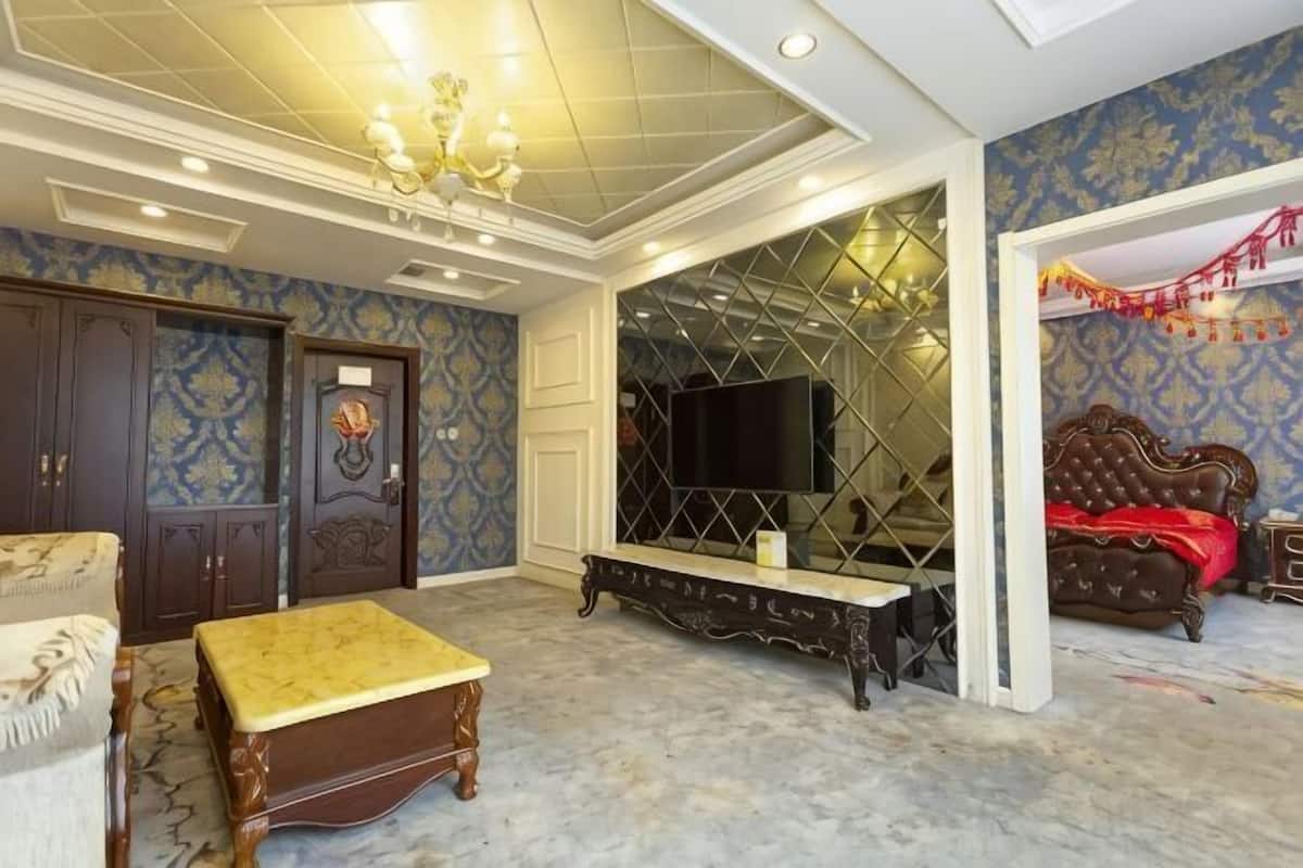 A room with a large bed, a television, a bench, and a door with a decorative handle.