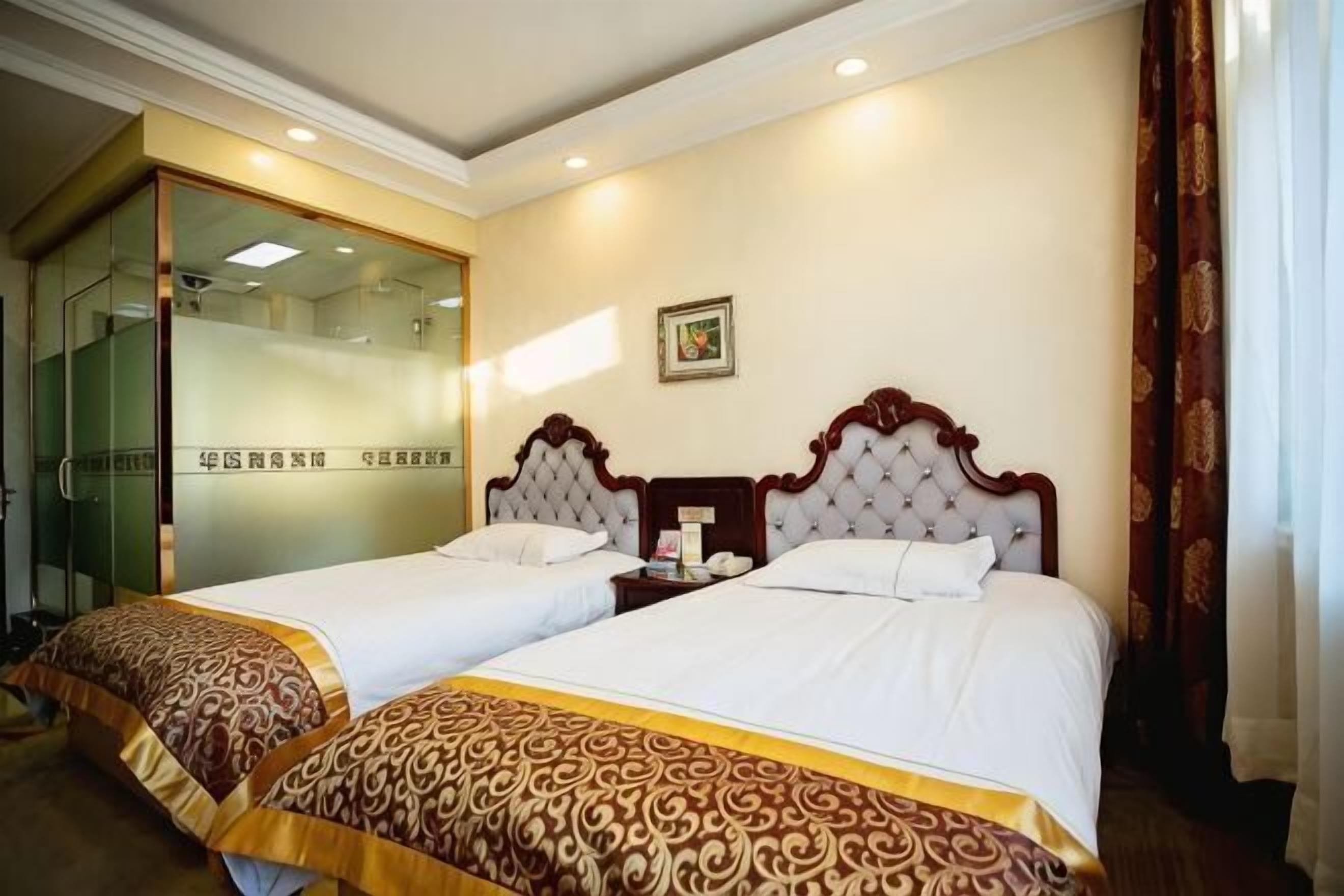 A hotel room with two beds, a glass door entrance, and a small bedside table.