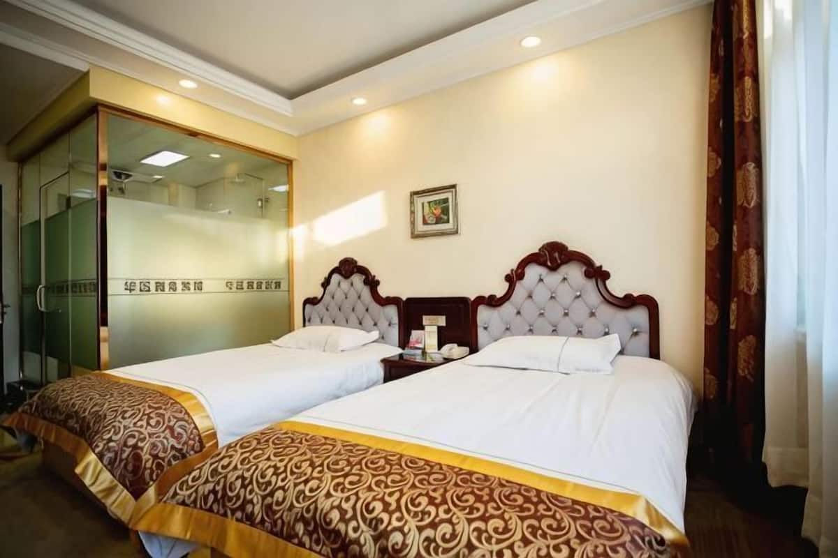 A hotel room with two beds, a glass door entrance, and a small bedside table.