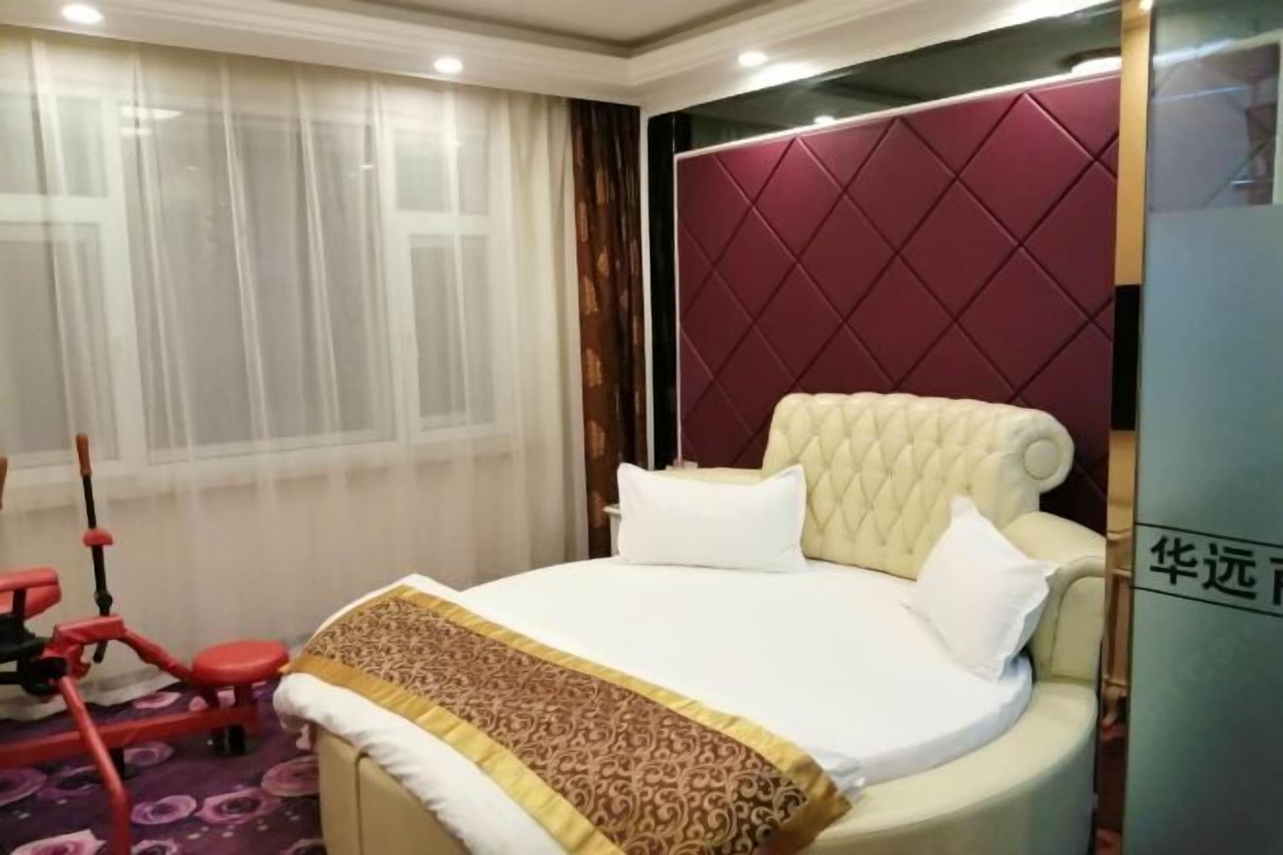 Une chambre d’hôtel avec un lit, un vélo d’exercice rouge et une grande fenêtre ornée de rideaux légers.