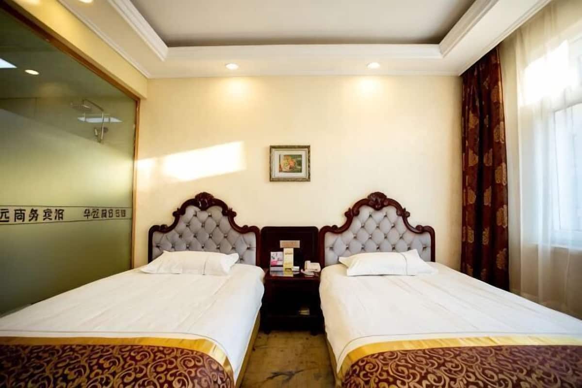 A hotel room with two beds, a nightstand, a framed picture on the wall, and a window with curtains.